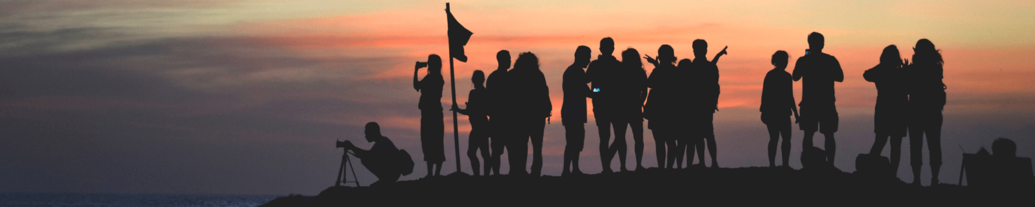 Über uns: Man sieht eine Gruppe von Menschen, die den Sonnenuntergang anschauen.